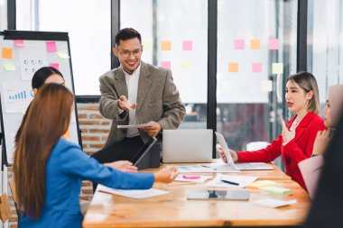 Çeşitli iş adamları ofis toplantısı sırasında verileri analiz ediyor ve stratejileri tartışıyor, belgeler ve dizüstü bilgisayar kullanarak..