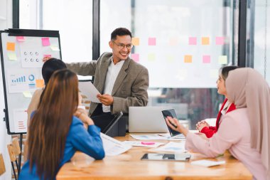 Çeşitli iş adamları ofis toplantısı sırasında verileri analiz ediyor ve stratejileri tartışıyor, belgeler ve dizüstü bilgisayar kullanarak..