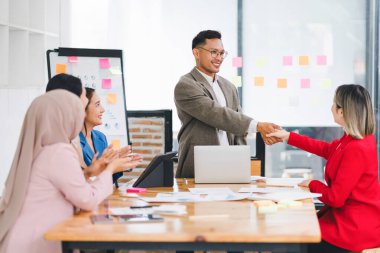 İş arkadaşları el sıkışıyor ve modern bir ofiste başarılı bir sunumu kutluyorlar.