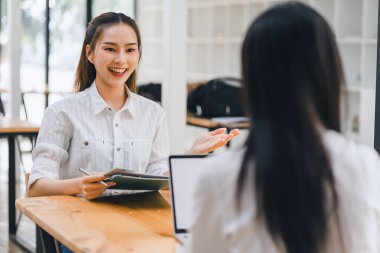 Bir projede birlikte çalışan iki bayan meslektaşım, beyaz bir masada üzerinde belgeler olan bir dizüstü bilgisayar kullanıyorlar..