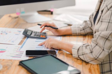 İşadamı, bir hesap makinesi ile bütçeyi hesaplıyor ve ahşap bir masadaki belgelerin finansal çizelge ve grafiklerini analiz ediyor..