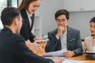 Çeşitli iş adamları ofis toplantısı sırasında verileri analiz ediyor ve stratejileri tartışıyor, belgeler ve dizüstü bilgisayar kullanarak..