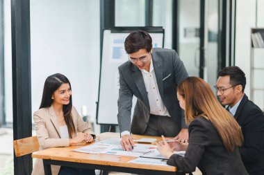Çeşitli iş adamları ofis toplantısı sırasında verileri analiz ediyor ve stratejileri tartışıyor, belgeler ve dizüstü bilgisayar kullanarak..