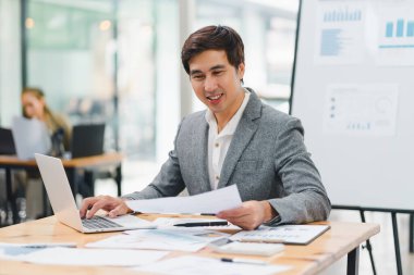 Modern ofiste bilgisayar ve belgelerle çalışırken kameraya gülümseyen kendine güvenen bir iş adamı.