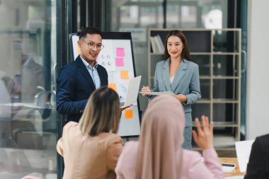 Çeşitli iş adamları ofis toplantısı sırasında verileri analiz ediyor ve stratejileri tartışıyor, belgeler ve dizüstü bilgisayar kullanarak..