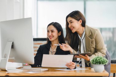 Modern ofiste bir proje üzerinde çalışan iki profesyonel Asyalı kadın.