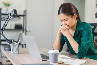Ev masasında çalışan stresli bir kadın, dizüstü bilgisayara ve ev işlerindeki görevlere bakıyor.
