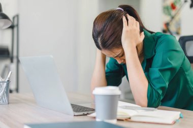Ev masasında çalışan stresli bir kadın, dizüstü bilgisayara ve ev işlerindeki görevlere bakıyor.