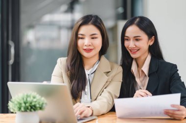 Modern ofiste bir proje üzerinde çalışan iki profesyonel Asyalı kadın.