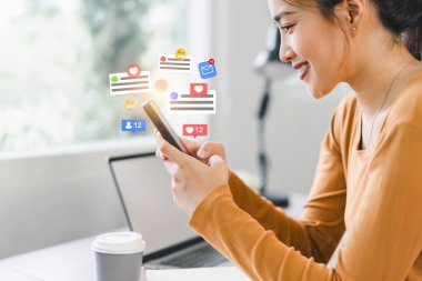 Güzel genç bir kadın cep telefonunda sosyal medyanın keyfini çıkarıyor. Bildirim simgeleriyle akıllı telefon ekranının üzerinde mesaj, yorum....