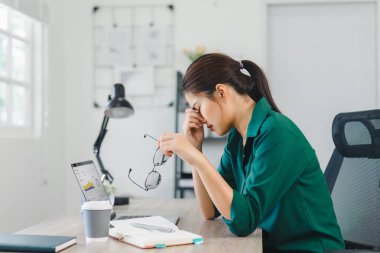 Ev masasında çalışan stresli bir kadın, dizüstü bilgisayara ve ev işlerindeki görevlere bakıyor.