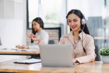 Kendine güvenen Asyalı genç kadın çağrı merkezi operatörü mikrofonlu kulaklık takıyor