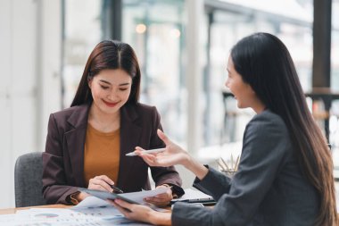 İki genç Asyalı iş kadını bir yatırım projesi ve planlama stratejisini tartışıyor ofiste dizüstü bilgisayarla çalışırken sohbet ediyorlar.