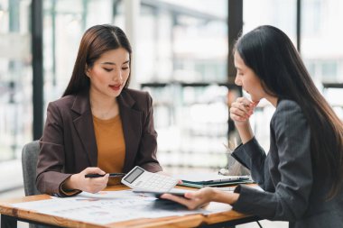 İki genç Asyalı iş kadını ofiste, planlama ve mali istatistikleri, yatırım piyasasını analiz ederek yeni bir başlangıç projesi fikrini tartışıyor.