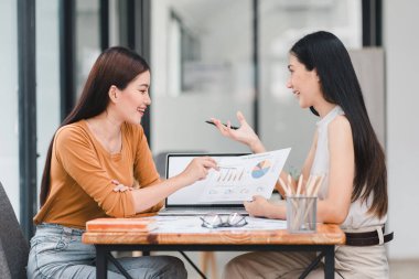 İki genç Asyalı iş kadını mali yönetim planlarını tartışıyor ve ofisteki yeni başlangıç projesi fikirlerini, mali planlamayı, istatistikleri ve yatırım piyasasını analiz ediyorlar.