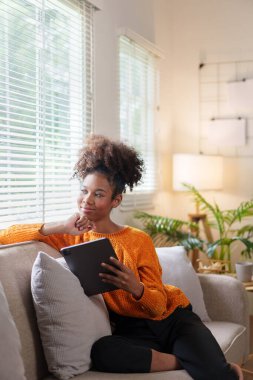 Tabletle kanepede dinlenen gülümseyen Afro-Amerikan kadın.