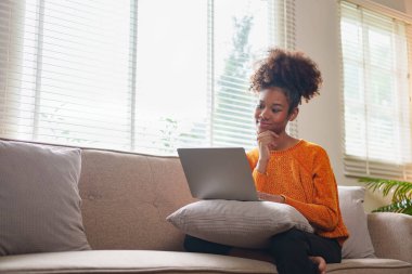 Evde dizüstü bilgisayarda çalışan genç Afrikalı Amerikalı kadın.