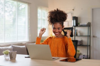 Gülümseyen Afro-Amerikan kadın bilgisayarlı ev ofisini parlak sabah ışığında kullanıyor.