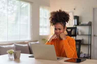 Samimi kazaklı genç siyahi kadın gün içinde ev ofisinde dizüstü bilgisayara konsantre oluyor.
