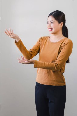 Neşeli Asyalı kadın elleri açık bir şekilde el kol hareketi yaparken gülümser ya da bir şeyi açıklar.