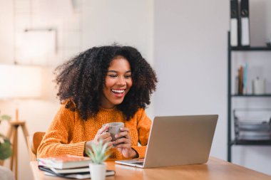 Gülümseyen Afrikalı Amerikalı kadın evde çalışırken dizüstü bilgisayar kullanıyor.