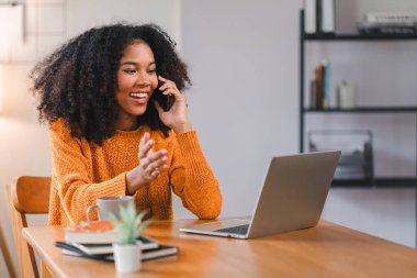 Afrika kökenli Amerikalı bir kadın bilgisayarla çalışırken telefonla konuşuyor.