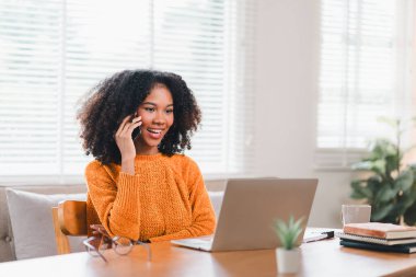 Güzel bir afro iş kadını ev ofisinin masasında oturarak arama yaparken çalışıyor. Uzak çalışma konsepti