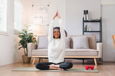 Rahat Afrika kökenli Amerikalı kadın evde yoga minderinde oturmuş kulaklıkla müzik dinliyor.