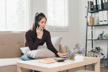 Evde dizüstü bilgisayar ve cep telefonuyla çalışan Asyalı genç bir iş kadını. İş hayatı dengesi kavramı