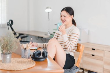 Bir kadın rahat bir ofiste dizüstü bilgisayarı üzerinde çalışırken bir fincan kahveden hoşlanır. parlak alan modern masa ve şık dekorlara sahip, verimli bir atmosfer yaratıyor..