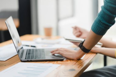 İşine odaklanmış, yakınındaki belgelerle birlikte ahşap masa üzerinde dizüstü bilgisayar kullanıyor..