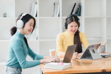 Laptoplar ve tabletlerle birlikte çalışan iki genç kadın, odaklanmış ve meşgul..