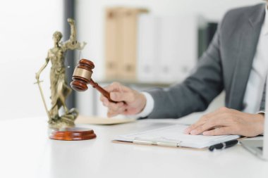 Hukuk bürosundaki tokmağı kullanarak adalet ve otoriteyi sembolize ediyor..