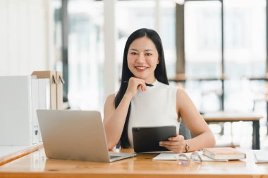 Kendine güvenen bir kadın modern ofis masasında çalışırken gülümser..