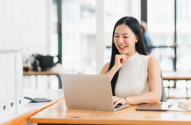 Modern ofiste dizüstü bilgisayarla çalışan profesyonel bir kadın gülümser..