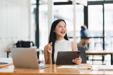 Modern çalışma alanında tablet kullanırken gülümseyen bir kadın.