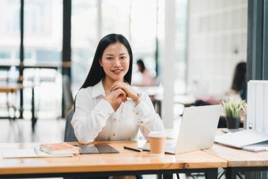 Kendine güvenen bir kadın modern ofiste masasında oturuyor, içten bir gülümsemeyle..