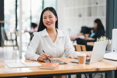 Masada çalışan, gülümseyen ve işleriyle meşgul profesyonel bir kadın..