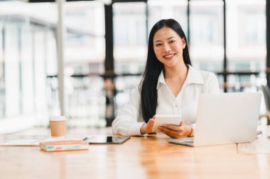 Profesyonel bir kadın modern ofis masasında çalışırken gülümser..