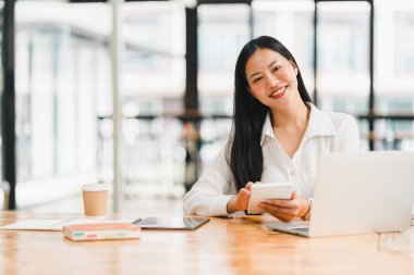 Profesyonel bir kadın modern ofis ortamında tablet kullanırken gülümser..