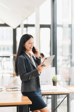 Modern ofiste tablet ve telefon kullanan takım elbiseli profesyonel bir kadın.