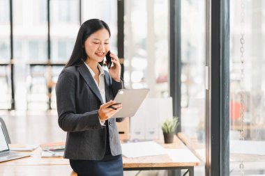 Ofiste tablet kullanan ve telefonla konuşan profesyonel bir kadın.