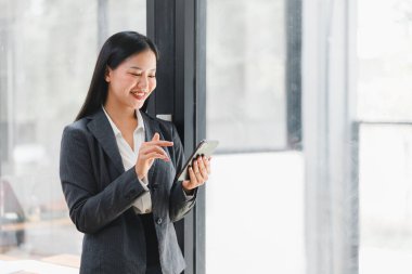 Bir iş kadını modern ofiste akıllı telefonunu kullanırken gülümser..