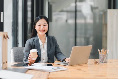 Ofiste çalışan profesyonel bir kadın, kahve fincanıyla gülümsüyor.