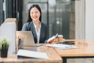 Profesyonel bir kadın masasında dizüstü bilgisayar ve kahveyle çalışırken gülümser..