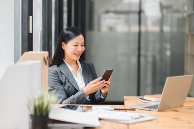 Profesyonel bir kadın modern ofiste akıllı telefonunu kullanırken gülümser..