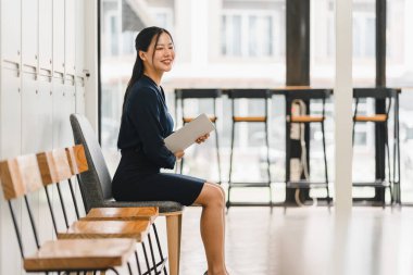 Profesyonel bir kadın, elinde defteriyle modern ofis alanında güvenle oturur..