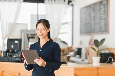 Modern kafe ortamında tablet kullanan gülümseyen bir kadın.