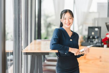 Kendine güvenen bir kadın elinde tabletle modern kafede duruyor ve gülümsüyor..