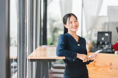 Kendine güvenen bir kadın modern kafede tablet tutarken gülümsüyor..